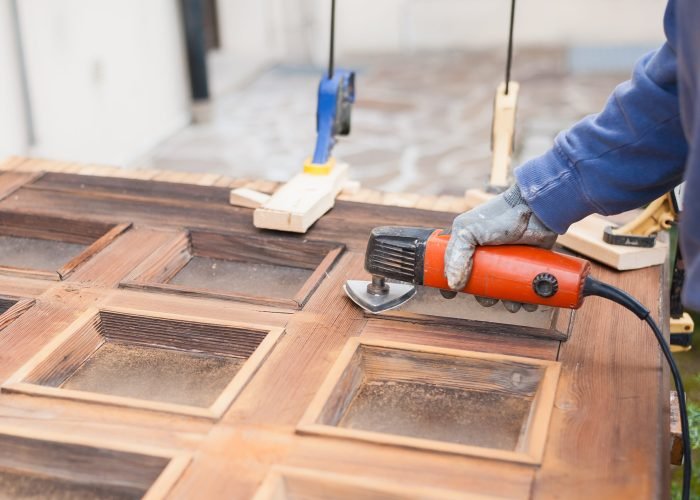 Carpenter at work with angular Sander. Maintenance and restoration of an old wooden door.
